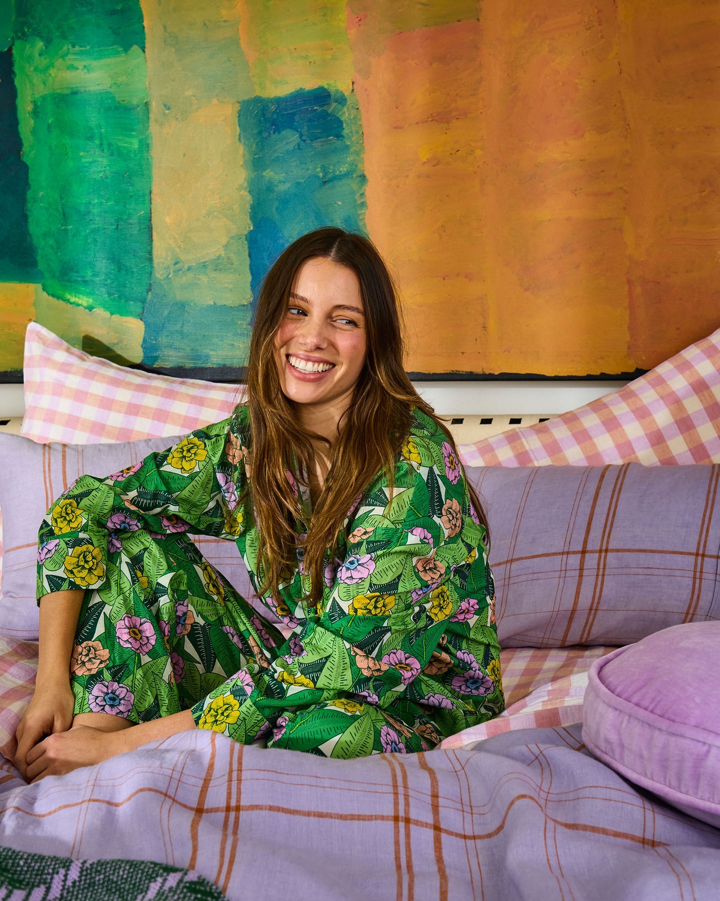 Woman in a floral green outfit sitting on a colorful bed with abstract art in the background