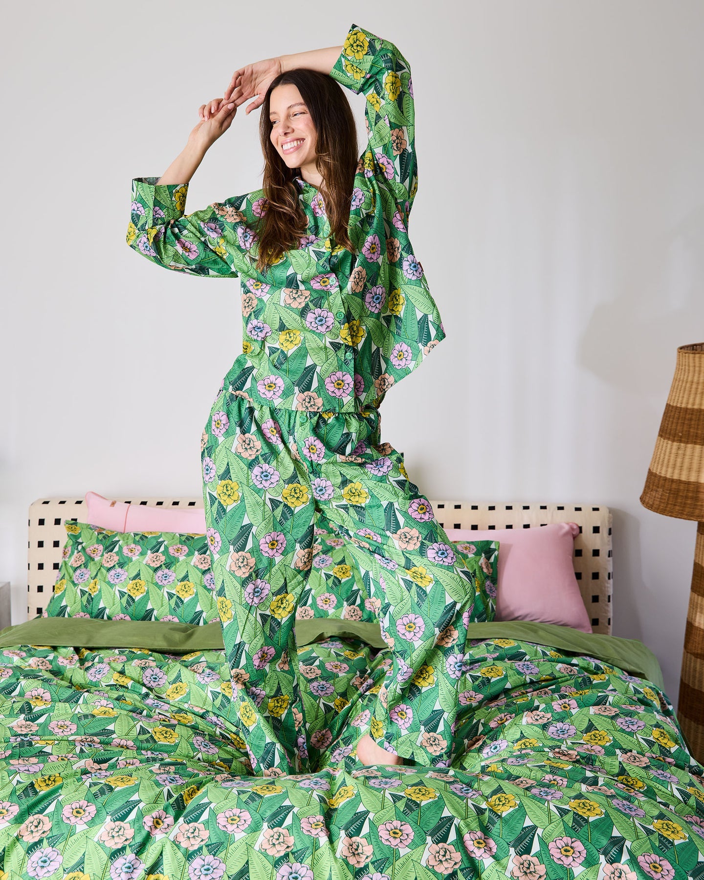 Woman in a green floral pajama set standing on a bed with matching bedding.