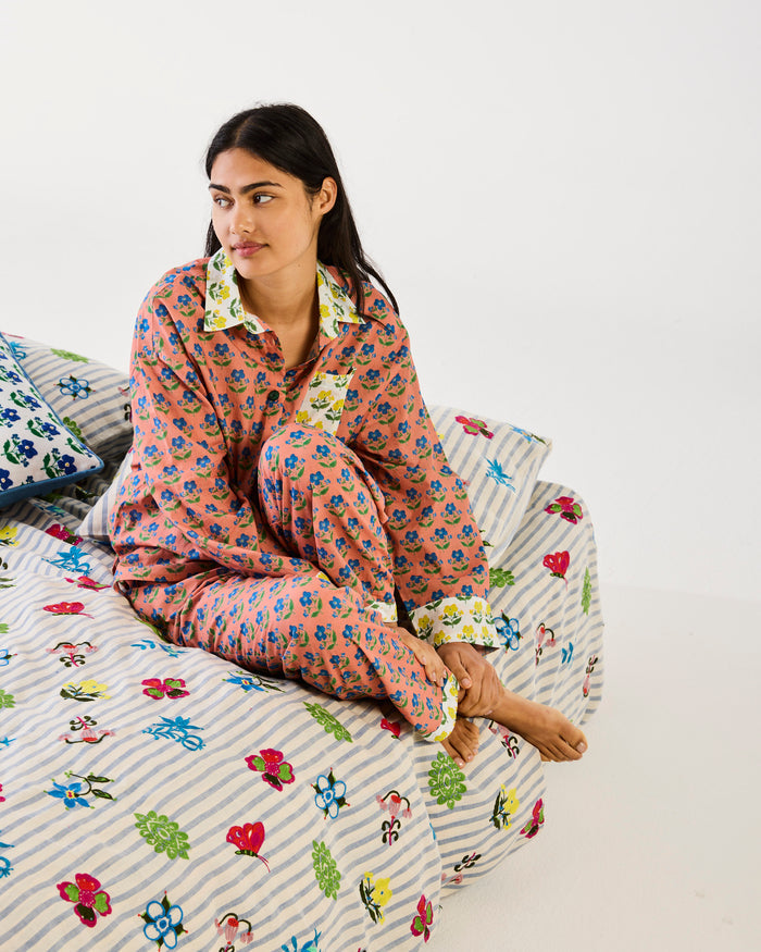 Woman wearing a floral pajama set sitting on a bed with matching bedding.