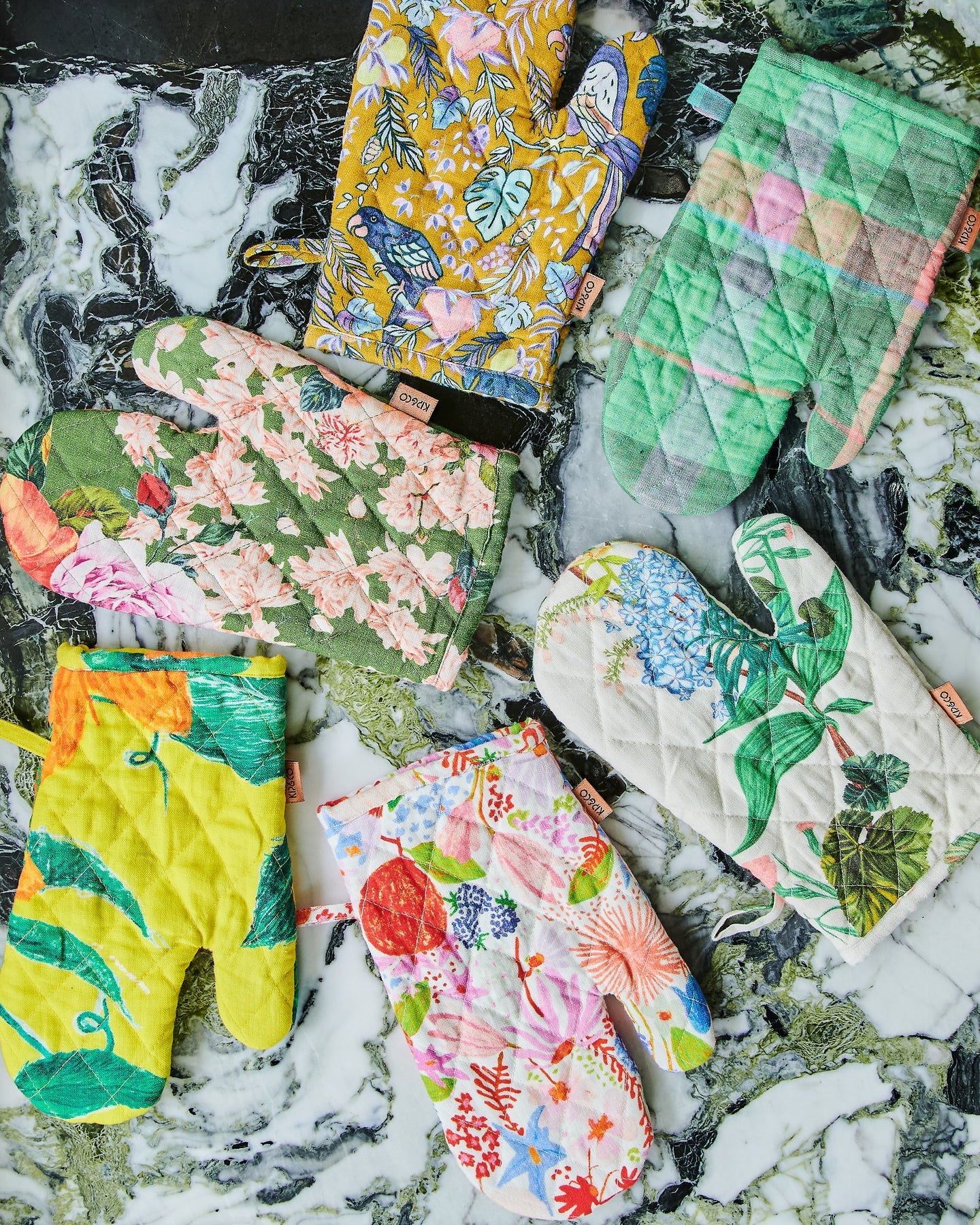 Oven mitts laid out on marble in assorted florals and patterns. 