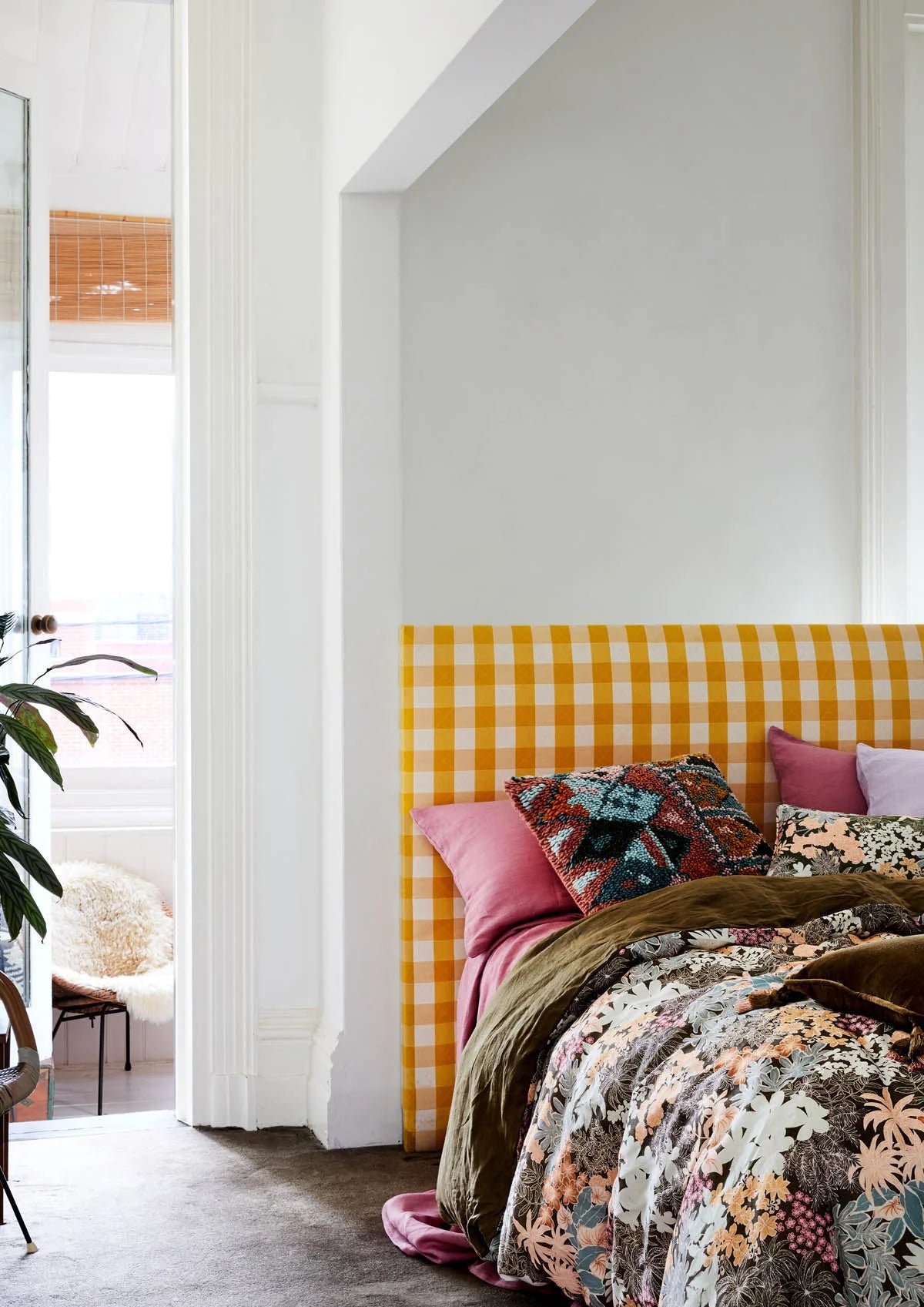 Bed with a yellow and white checkered headboard in a room with a white wall and a plant.