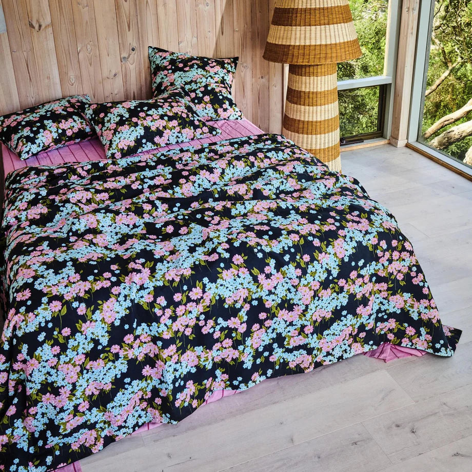 Floral bedding set on a bed in a room with wooden walls and a lamp.