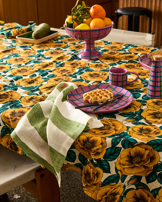 Table setting with a floral tablecloth, waffle on a plate, and fruit bowl.