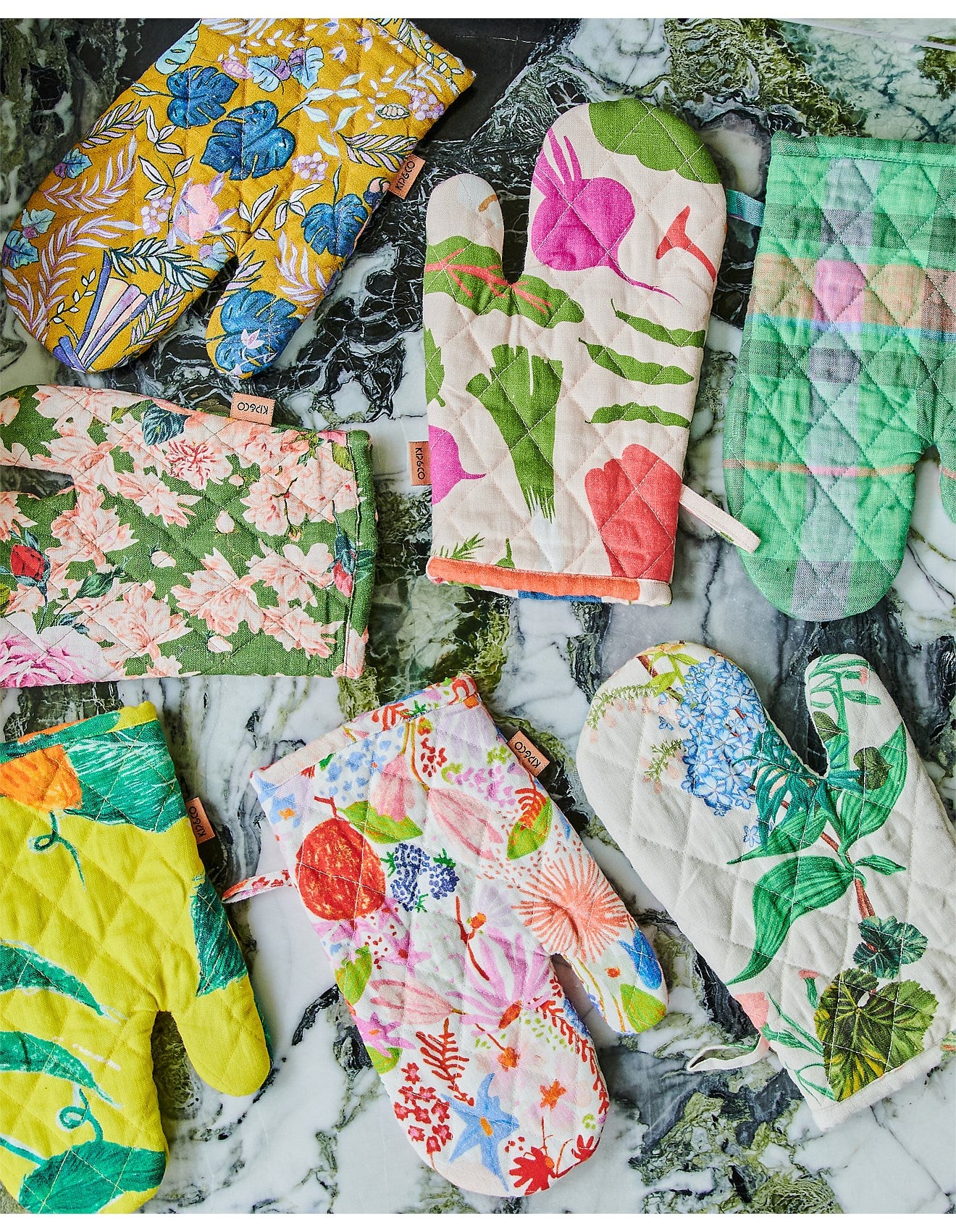 Collection of colorful quilted oven mitts  with floral and leaf patterns on a marble surface.