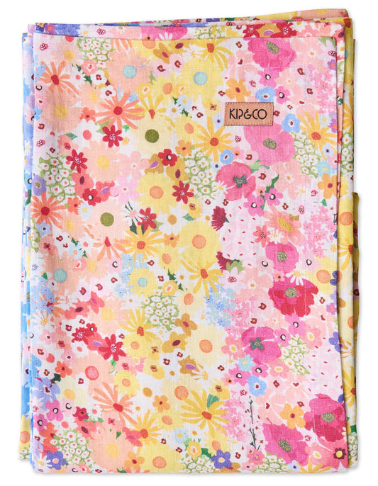 A folded fabric tablecloth featuring a vibrant multicolor floral pattern on a light pink background. A small brown leather brand tag reading 'KIP&CO' is stitched near the top center.