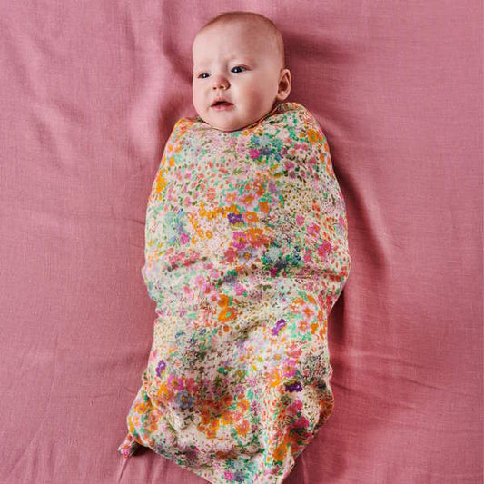 Baby wrapped in a colorful floral blanket on a pink surface