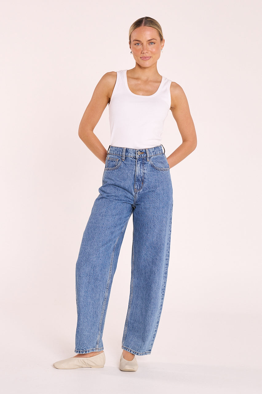 Woman wearing a white tank top and blue jeans on a plain background