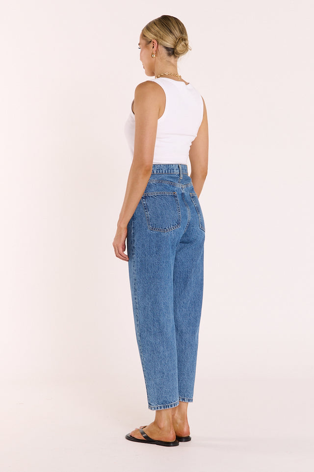 Woman wearing blue jeans and a white top on a light pink background