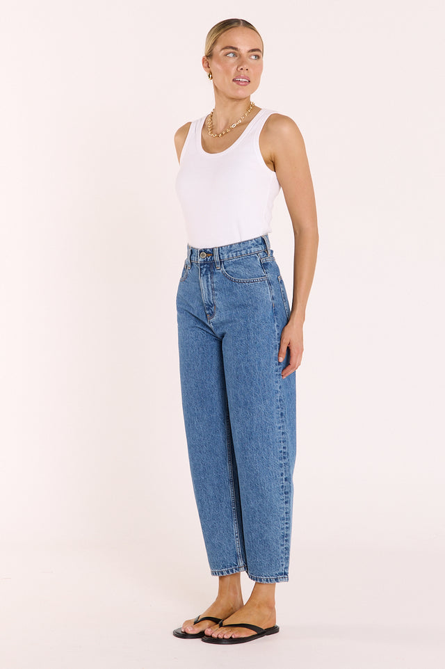 Woman wearing a white tank top and blue jeans on a plain background