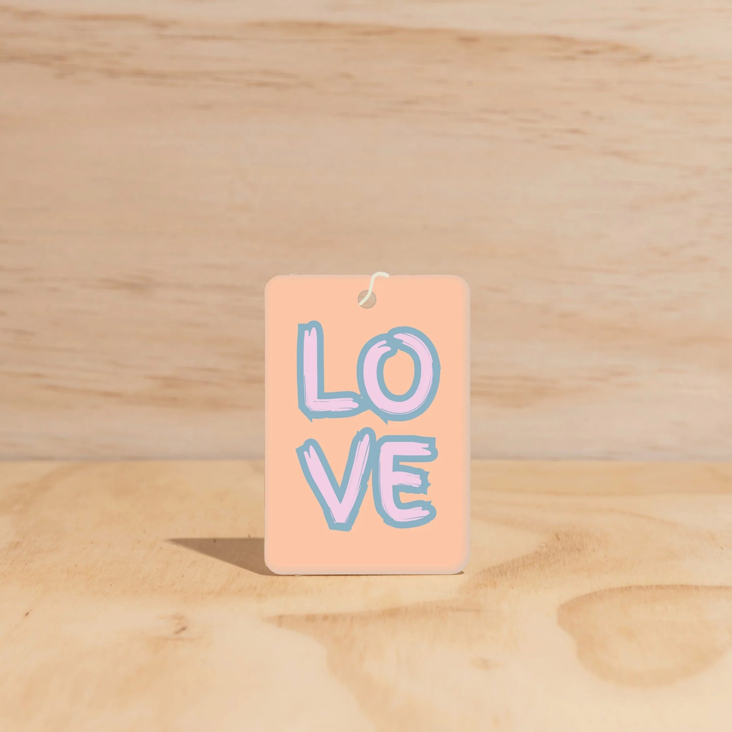 Rectangle car freshener with 'LOVE' text written on front in bold letters. Peach background with pink and blue lettering. 
