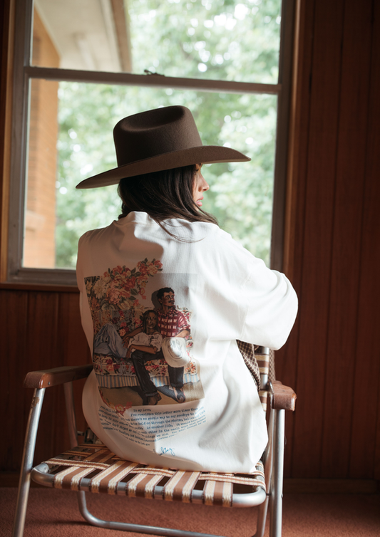 Person wearing a white shirt with a printed design, sitting on a chair indoors.