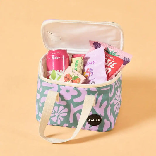 A Kollab insulated lunch bag with a retro floral pattern in sage green and lavender, shown open and filled with snacks and drinks on a solid peach background.
