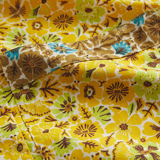 A close-up of a folded piece of fabric with a retro floral pattern in yellow, brown, green, and light blue on a white background.