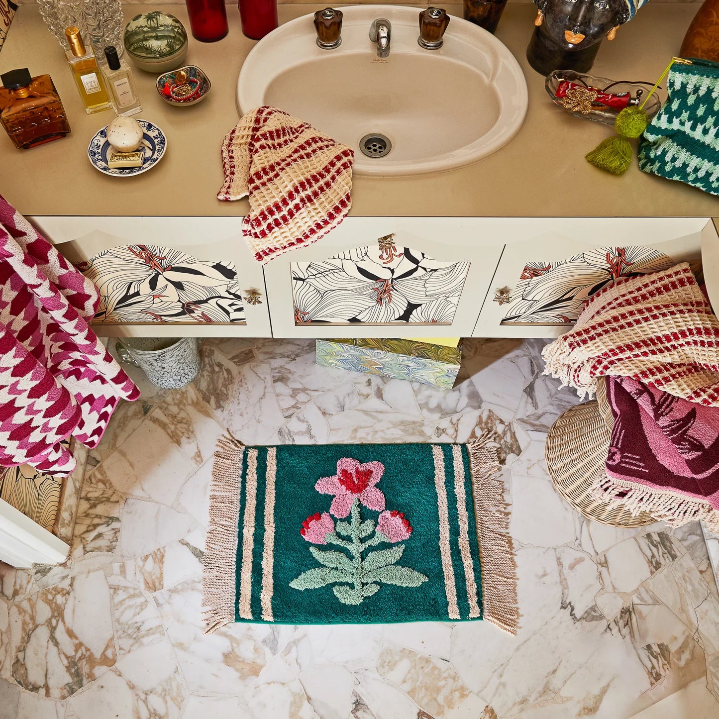 Bathroom counter with decorative items and a floral bath mat on the floor.