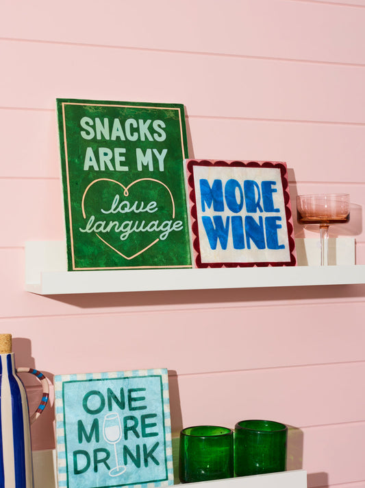 Three signs with humorous sayings on a shelf against a pink wall.