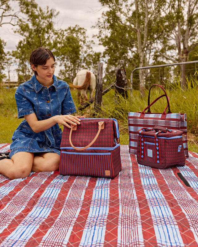 Woman sitting on a picnic blanket with plaid bags in a natural setting