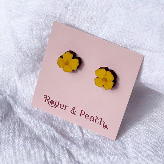 Yellow flower earrings on a pink card with 'Roger & Peach' branding, on a white fabric background.