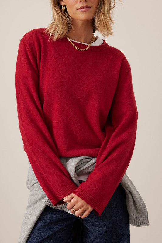 Person wearing a red sweater over a gray shirt with a neutral background