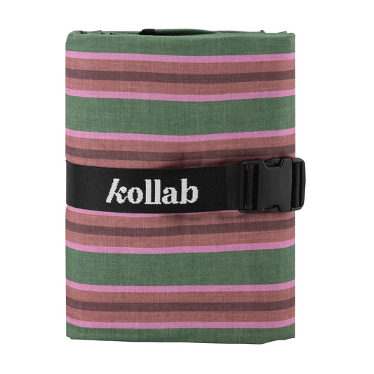 Picnic mat sits with white background and black strap holding together. Colours within mat are green, brown and pink with striped pattern.