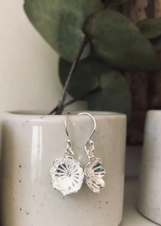 Silver earrings on a white ceramic surface with green leaves in the background
