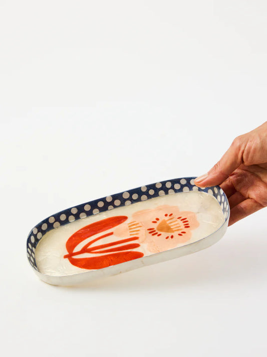 Hand holding a decorative ceramic tray with floral design on a white background
