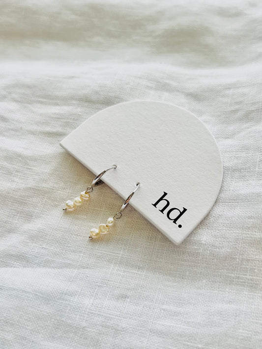 Pearl earrings on a white jewelry pouch with 'hd.' text on a light fabric background