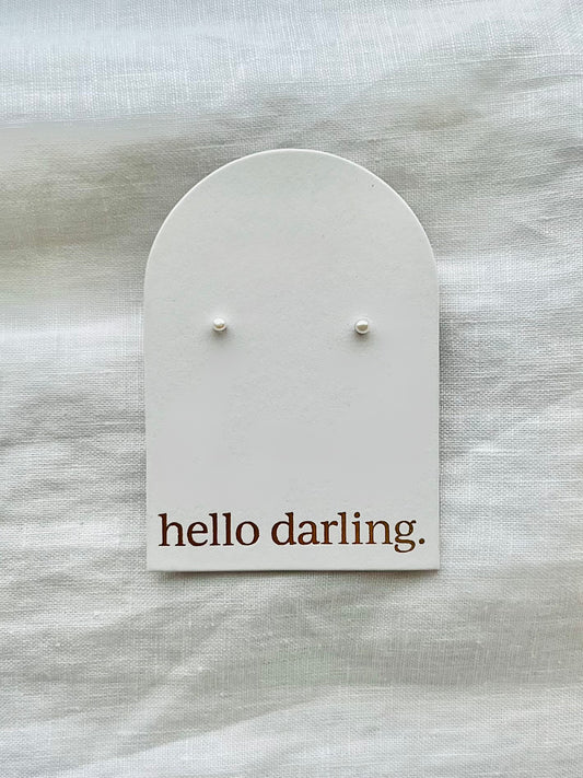 Pair of petite pearl earrings on a 'hello darling' card against a textured white background