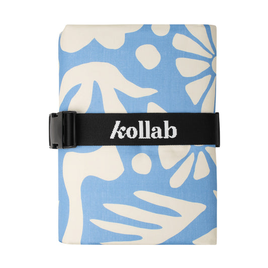 Folded picnic mat with blue and white leaf pattern and 'kollab' branding on a black strap.