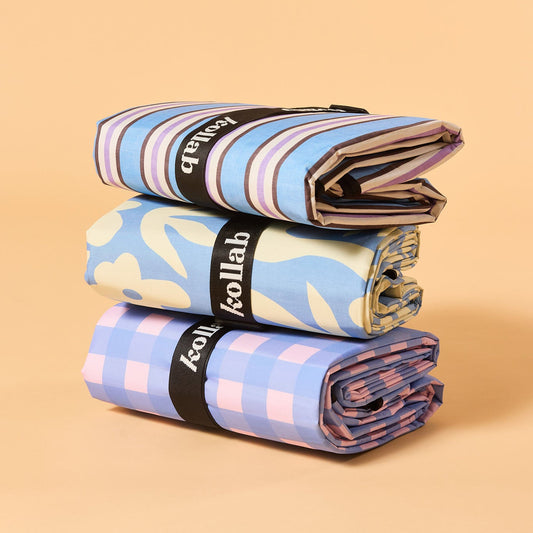 Three rolled fabric items stacked vertically on a warm beige background. Each roll is wrapped with a black band featuring the white 'kollab' logo.