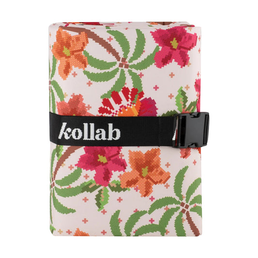 A rolled-up travel or packing cube with a colorful pixelated floral and palm tree pattern on a light pink background, secured with a black strap featuring the white 'kollab' logo.