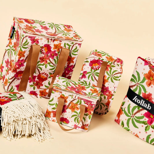 A coordinated set of Kollab insulated tote bags and cooler bags with a colorful floral print on a cream background, brown handles, and a macrame bag with fringe, arranged on a warm beige studio background.