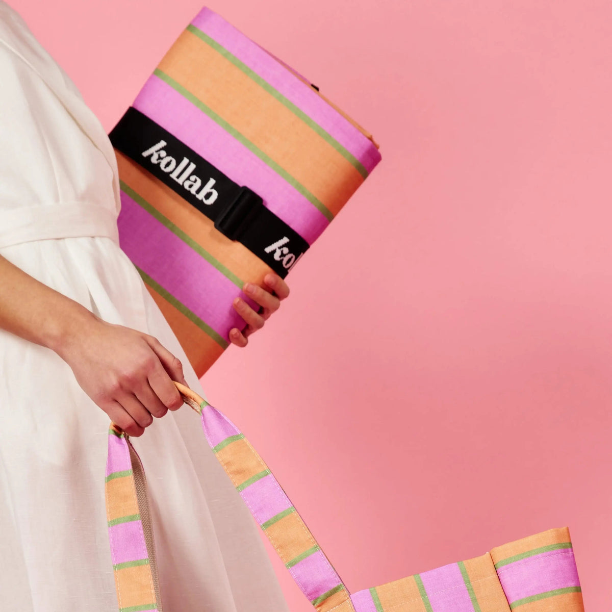 Woman holds picnic mat in one hand and carryall bag in the other. 