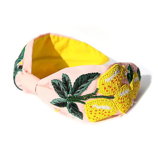 A beaded headband with a vibrant, colorful design, featuring leaf patterns and a prominent yellow element on a pink band.