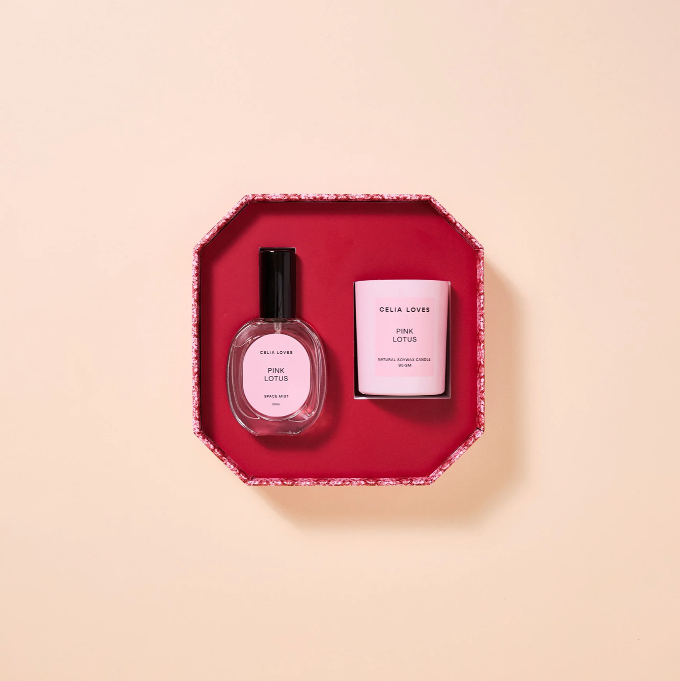 Two beauty products, a room spray and a candle, in a red hexagonal tray on a beige background.