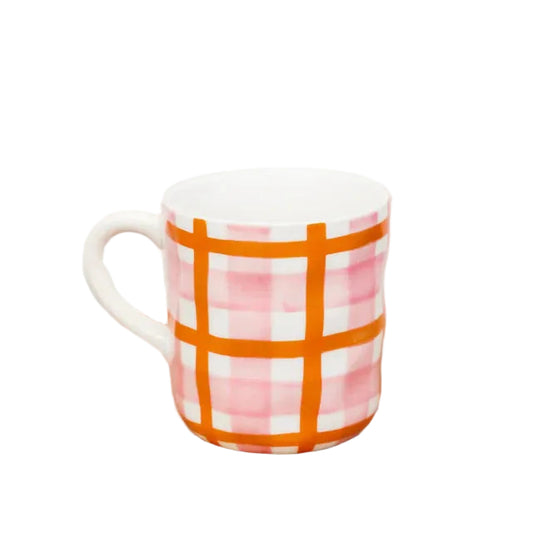 White mug with pink and orange plaid pattern on a wooden surface