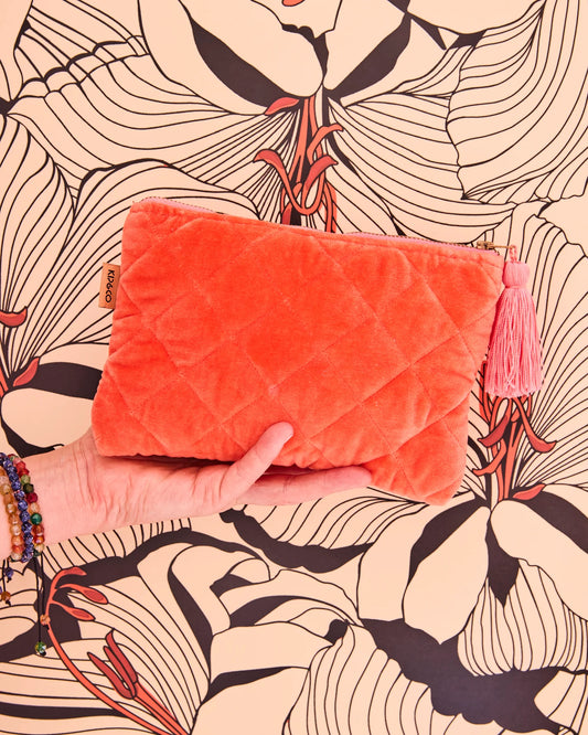 Orange quilted pouch with a tassel held against a patterned background