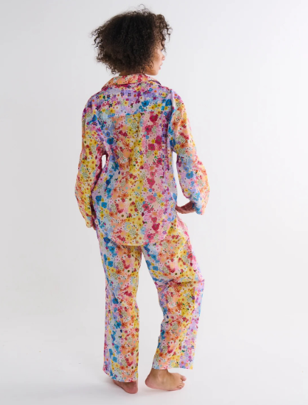 A woman wearing a two-piece pajama set with a colorful floral print, shown from the back against a plain white studio background.