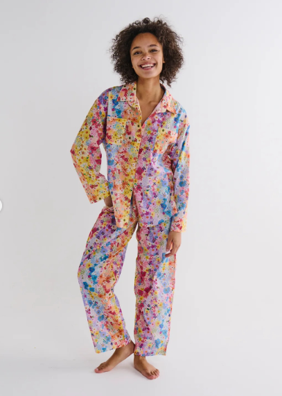 A woman modeling a two-piece pajama set with a vibrant multicolor floral print, standing against a plain white studio background.