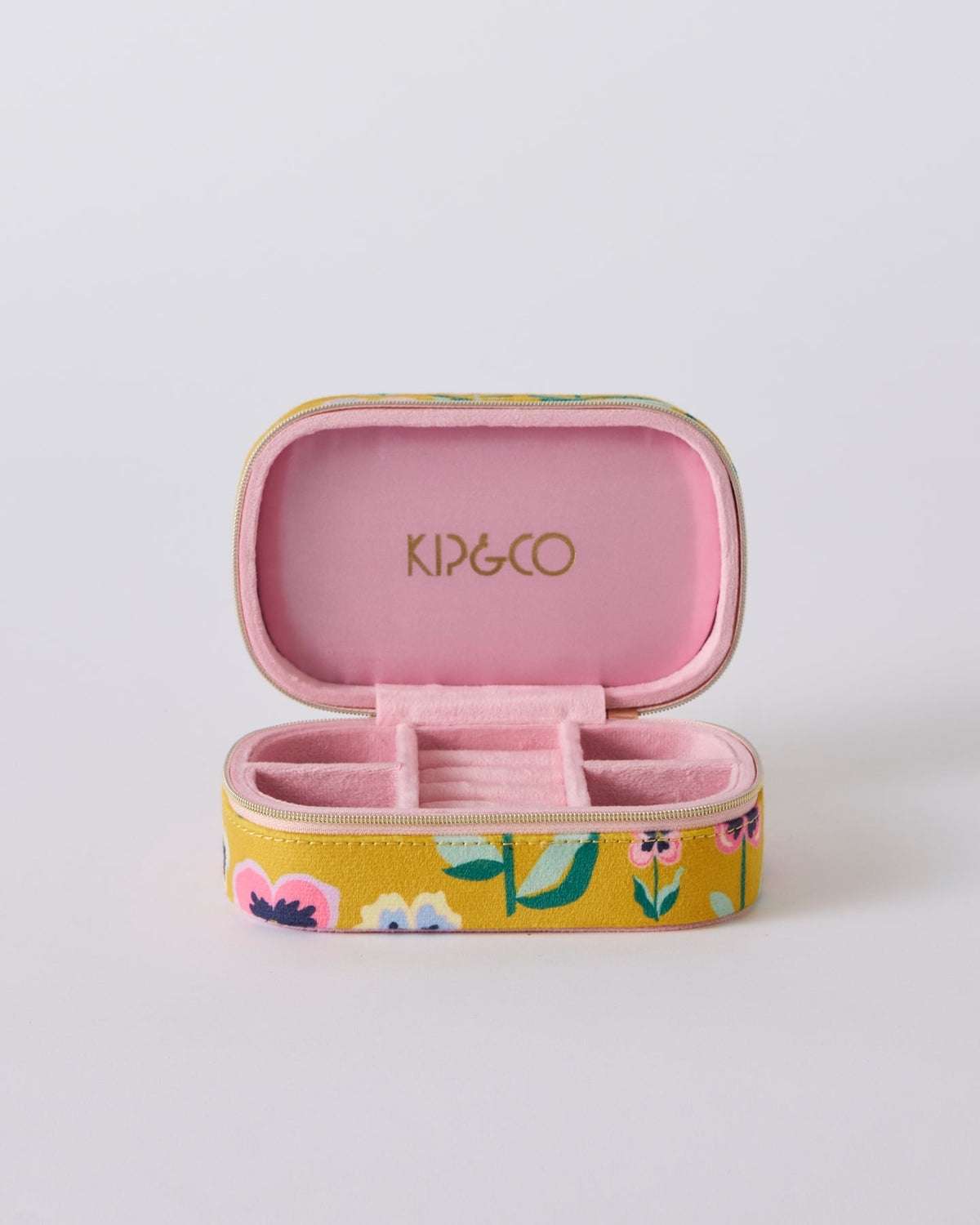 An open KIP&CO jewelry case with a yellow floral exterior and a pink interior, showing the brand name in gold on the lid.