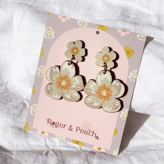 Cream floral earrings on a 'Roger & Peach' branded card against a white fabric background