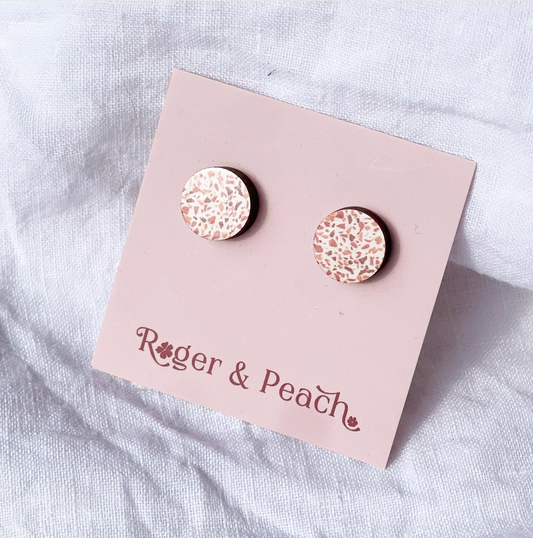 Round earrings with a granite like pattern on a 'Roger & Peach' branded card against a light fabric background.