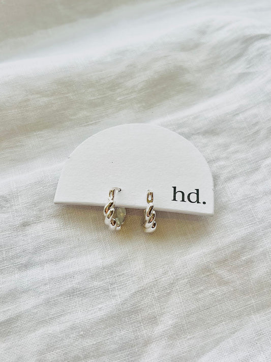 Silver hoop earrings on a white jewelry card with 'hd.' text, placed on a textured white surface.