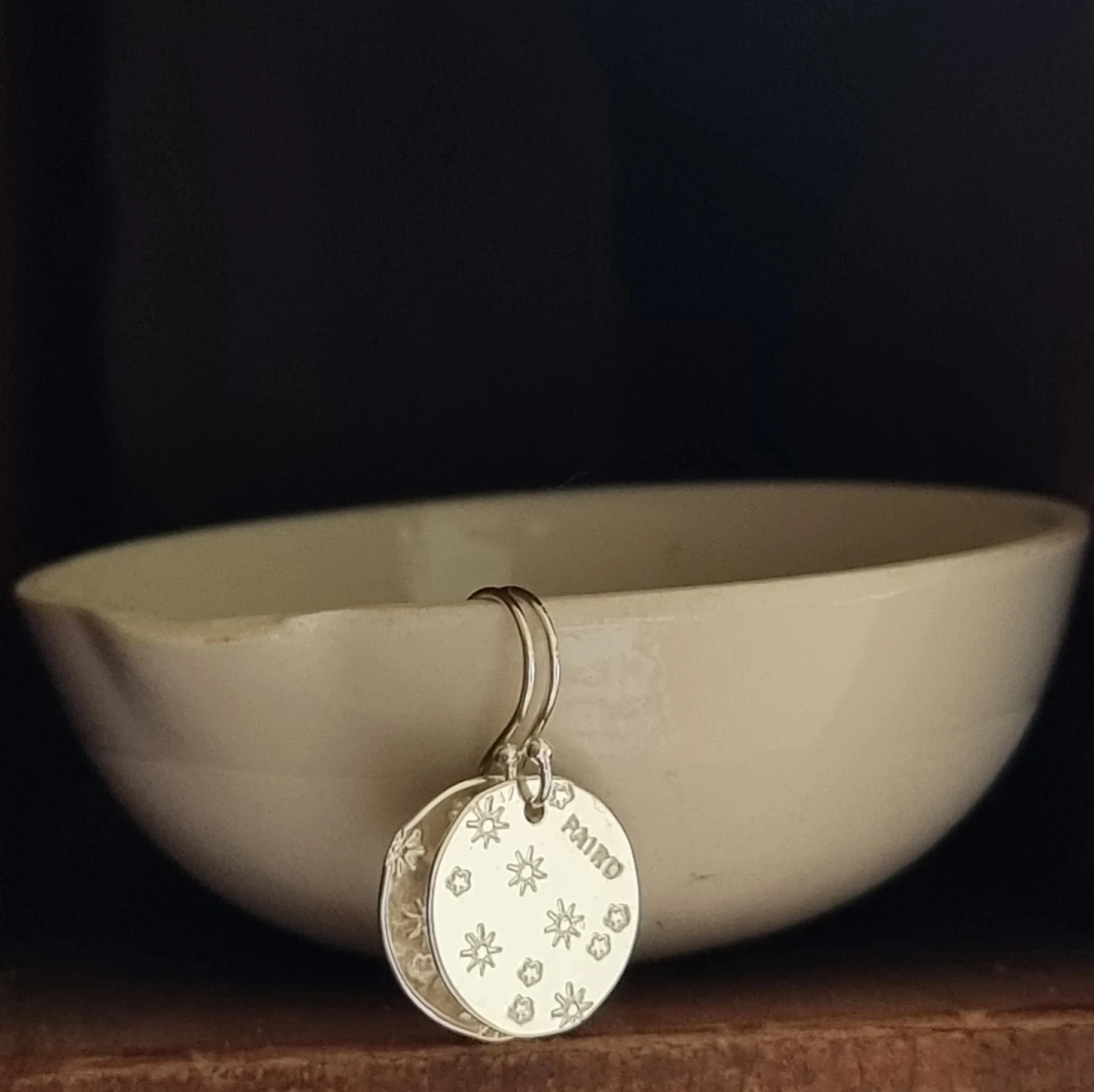 Silver circle disc earring with engraved flower design on a dark background.