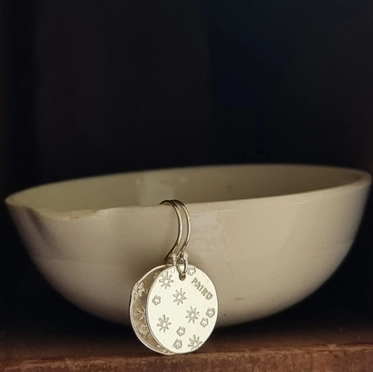 Silver circle disc earring with engraved flower design on a dark background.