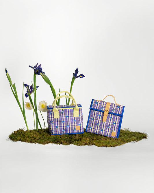 Two patterned picnic-style tote bags displayed on a patch of moss with decorative iris flowers against a clean white studio background.