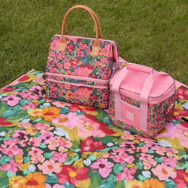 A floral picnic bag and matching cooler bag placed on a matching floral blanket on green grass.