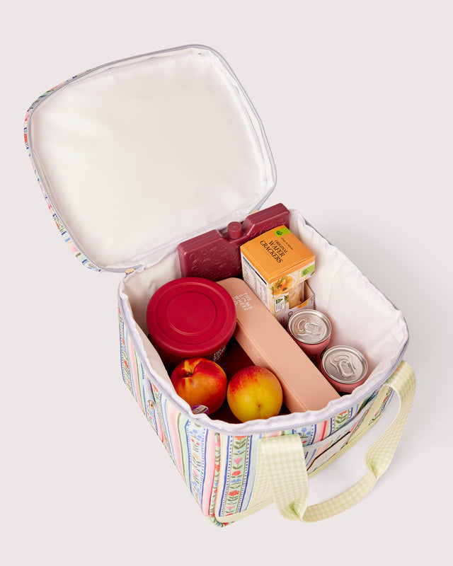 A pastel patterned lunch bag with a white insulated interior, shown open and filled with snacks and fruit on a light gray background.