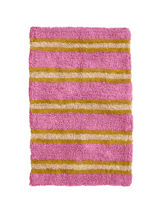 Pink bath mat with gold and beige stripes on a green background