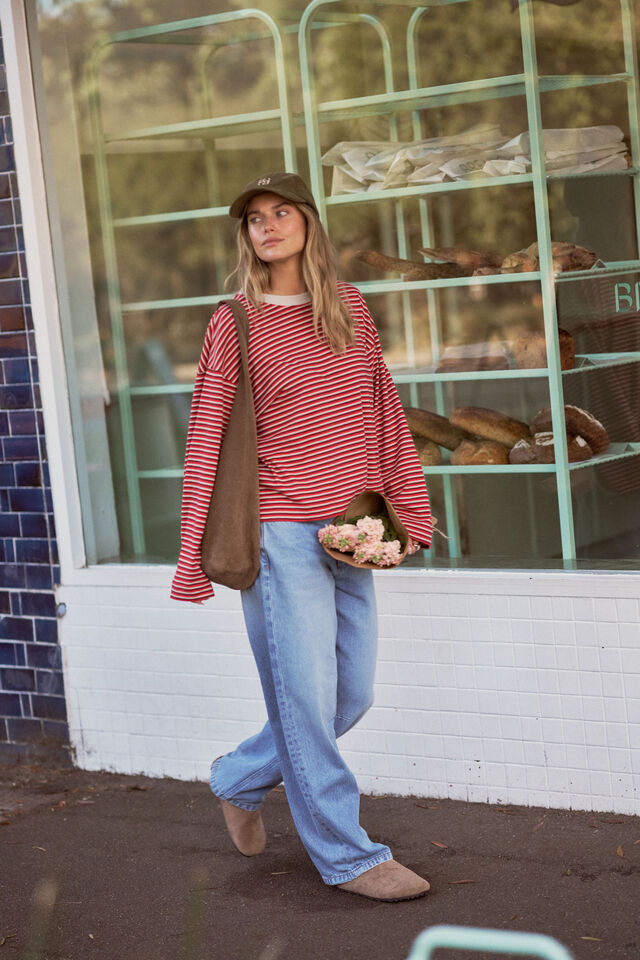 Woman in a red striped shirt and blue jeans standing outside a bakery.