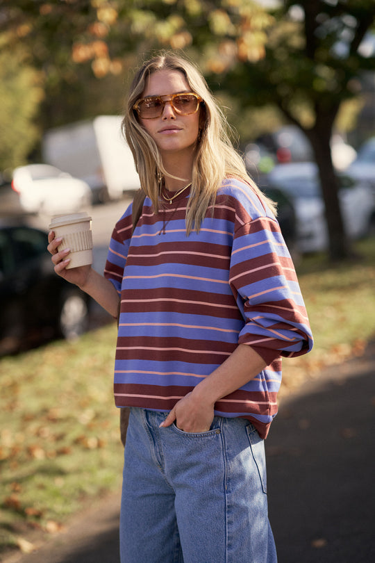 Woman wearing a striped sweater and sunglasses, holding a coffee cup outdoors.